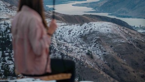 A person sitting on a swing overlooking a mountainous landscape with a lake.