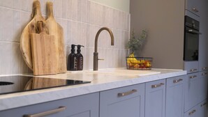 A modern kitchen with a marble countertop, a stainless steel sink, wooden cutting boards, and a fruit basket. - Julia's Holidayhome (Egmond-Binnen)