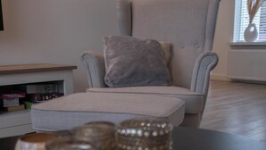 A modern living room with a grey armchair, a small ottoman, and a table with decorative items. - Julia's Holidayhome (Egmond-Binnen)