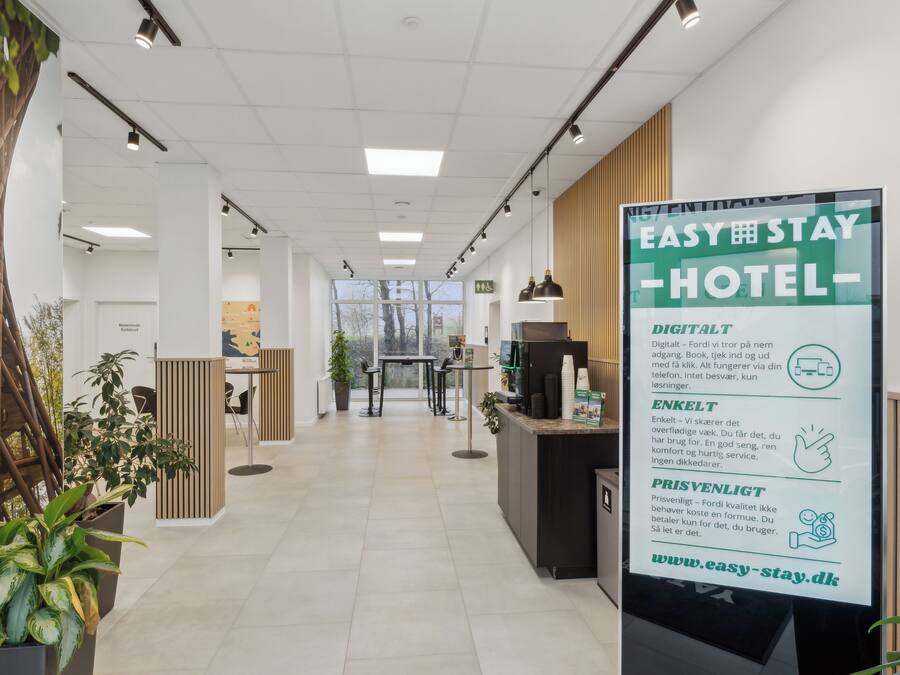 A modern hotel reception area with a digital signboard, reception desk, and potted plants.