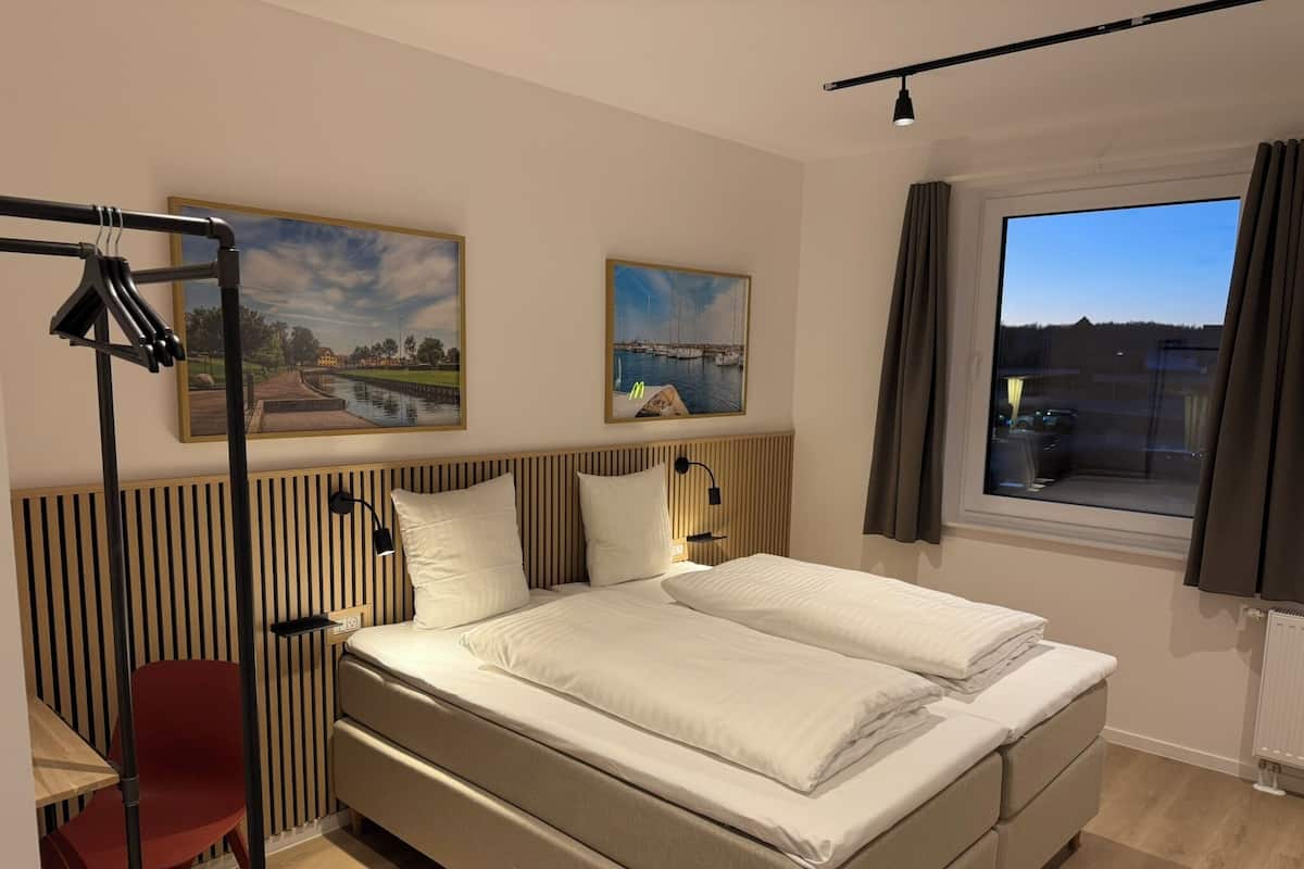 Ett modernt hotellrum med en säng, ett skrivbord, en stol och två tavlor på väggen.