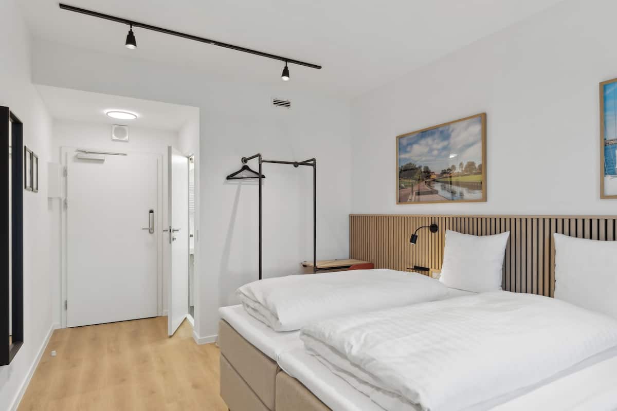 Ett modernt hotellrum med en stor säng, en sänggavel i trä, en tavla och ett skrivbord med en stol.