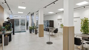 Un espacio de oficina moderno con área de recepción, mesas de reuniones y plantas en macetas.