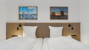 Una cama doble con cabecera de listones de madera, dos mesitas de noche con lámparas y dos cuadros enmarcados en la pared.