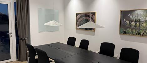 Une salle de conférence avec une longue table, six chaises et deux lampes suspendues.