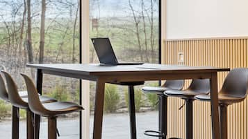 Une chambre moderne avec une grande fenêtre, un ordinateur portable posé sur une table et trois tabourets de bar.
