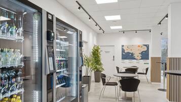 Un hall d’hôtel moderne doté d’un espace de service en libre-service pour les boissons, d’une grande carte affichée au mur et d’un coin salon avec des tables et des chaises.