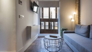 Una sala de estar moderna con un sofá gris, una mesa redonda de estructura metálica y un televisor montado en la pared.