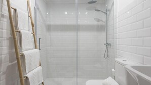 Un baño moderno con azulejos blancos tipo metro, un box de ducha de vidrio, un toallero de bambú y un inodoro blanco.
