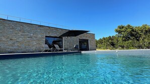 Un área de piscina moderna con agua cristalina, paredes de piedra y sillones de descanso.