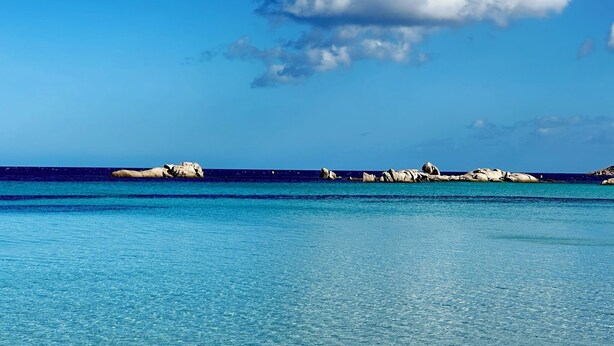 Un mar azul transparente con aguas tranquilas y afloramientos rocosos a lo lejos.