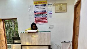 A hotel reception area with a reception desk labeled "RECEPTION," a wooden counter, and a wall with hotel rules and a phone number. - Hotel Star Marigold (New Delhi)