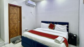 A bedroom with a bed, a ceiling fan, an air conditioning unit, and a wooden door. - Hotel Star Marigold (New Delhi)