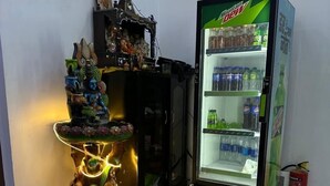 A room with a decorative altar, a Mountain Dew refrigerator, and a fire extinguisher. - Hotel Star Marigold (New Delhi)