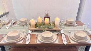 Une table à manger dressée avec de l’assiette blanche, des bols, des couverts et des bougies, et une petite lanterne placée au centre.