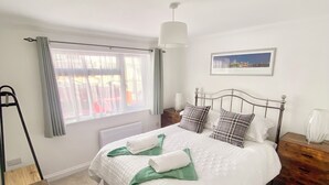 Une chambre bien rangée, avec un lit, des tables de chevet, une lampe et une fenêtre avec des rideaux.