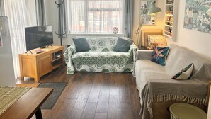 Un salon comprenant un canapé, un téléviseur, un meuble en bois, une fenêtre avec des rideaux et une lampe.