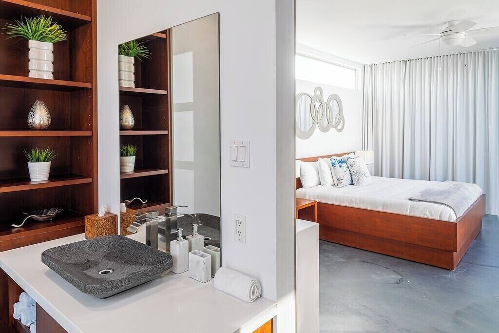 A modern bathroom with a large mirror, a granite sink, and shelves with decorative items. The bathroom features a wooden vanity and a white countertop.