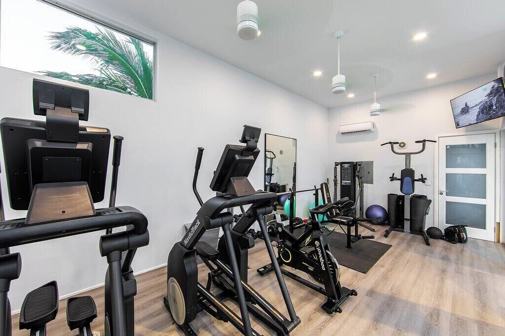 Une salle de sport moderne équipée de machines de cardio, de poids libres et d’un miroir.