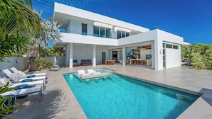 Una casa moderna de dos pisos con piscina, mobiliario exterior y una escalera que lleva al piso superior.