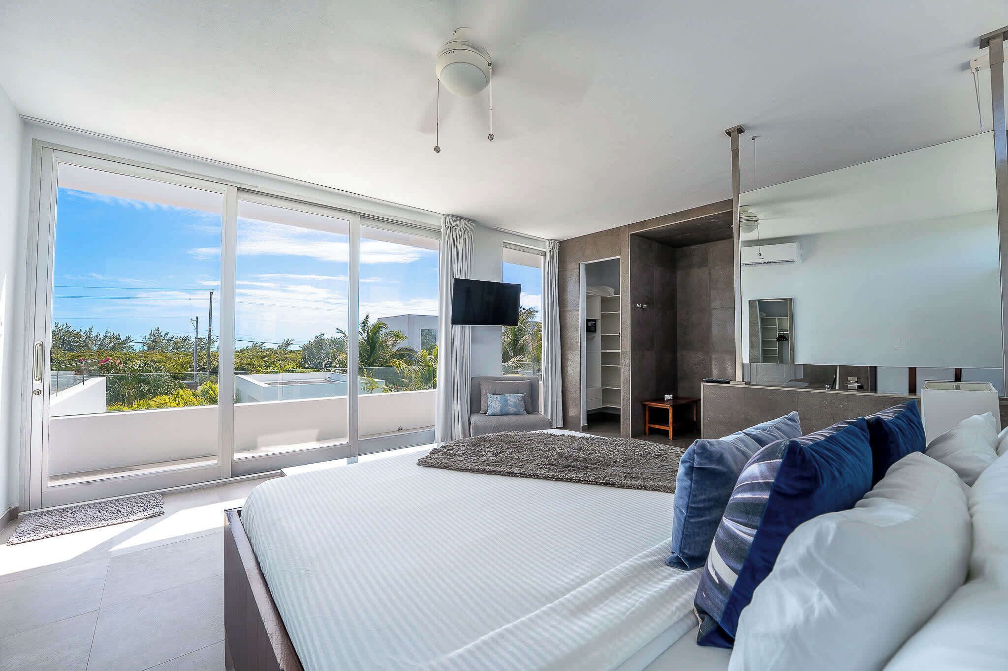 A modern bedroom with a large bed, a TV, and a balcony with a view.