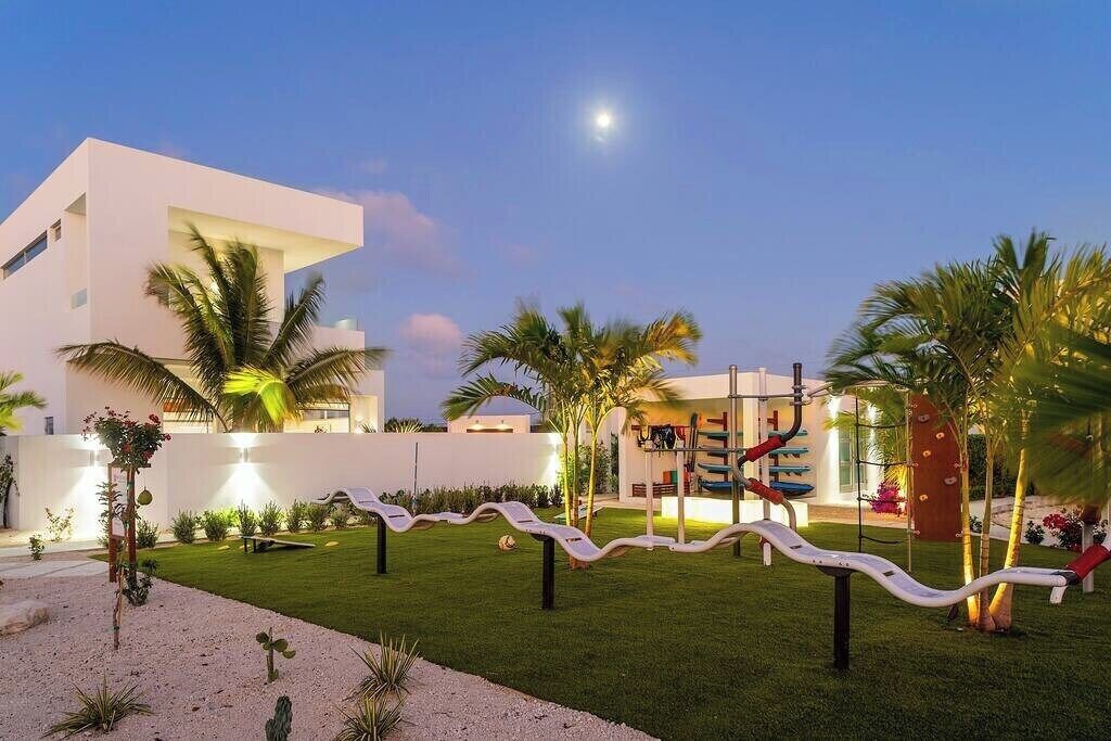 A modern building with a white exterior, a well-maintained lawn, and a series of outdoor exercise equipment.