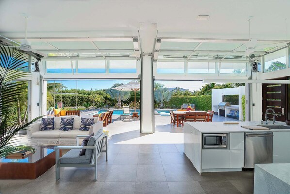 A modern kitchen with a large island, a dining area with outdoor seating, and a view of a pool and mountains.