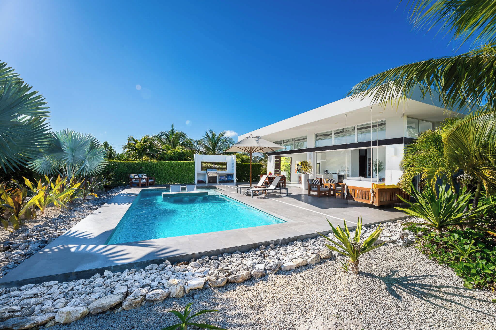 A modern house with a swimming pool, outdoor seating, and lush landscaping.