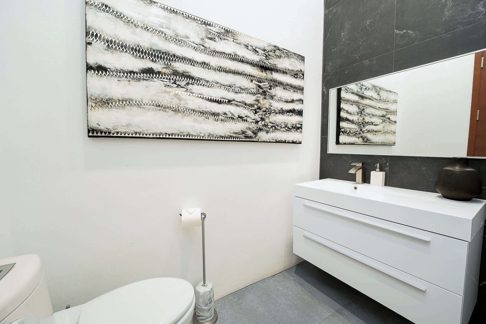 Casa de banho moderna com toucador branco, um espelho grande e uma obra de arte abstrata a preto e branco na parede.