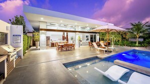 A modern house with a swimming pool, outdoor dining area, and a barbecue setup. - Family Beachside Villa With Hotel Amenities v7 (Providenciales)