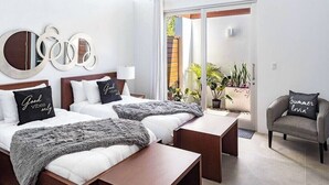 A modern hotel room with two beds, a sofa, and a balcony with plants. - Family Beachside Villa With Hotel Amenities v7 (Providenciales)