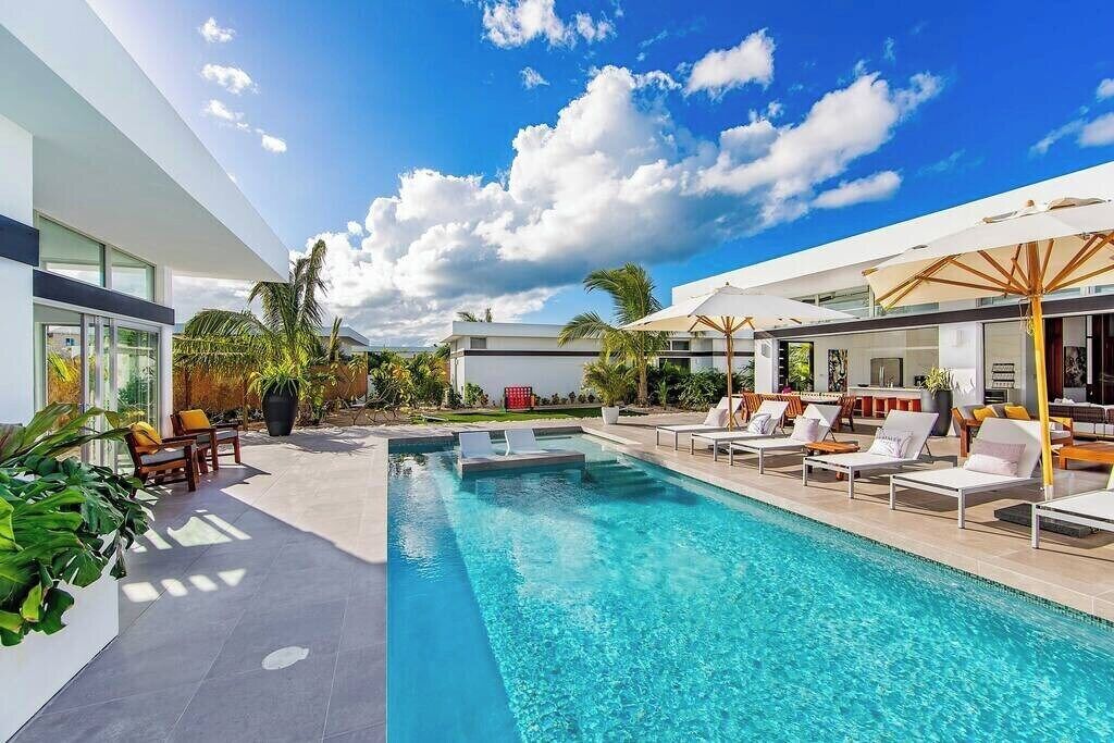 Ein moderner Poolbereich mit klarem, blauem Wasser, Liegestühlen und einem zeitgemäßen Gebäude mit großen Fenstern.