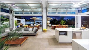 A modern open-plan living area with a kitchen, dining space, and a view of the outdoors. - New Seaside Vacation Villa With Hotel Amenities v9 (Providenciales)