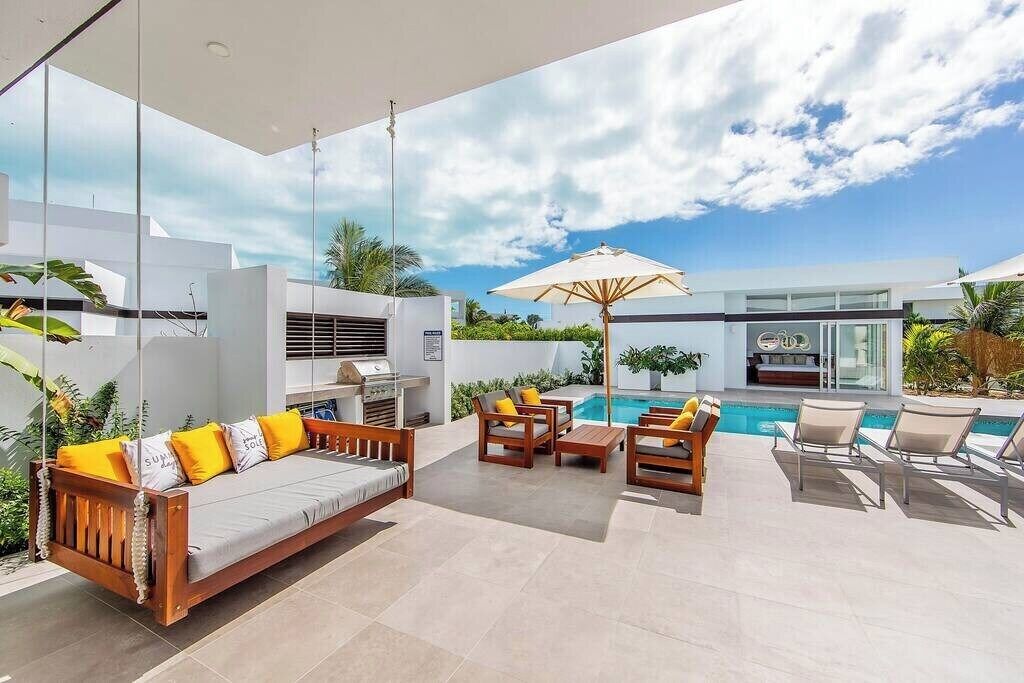 An outdoor living area with a sofa, chairs, a pool, and a grill.