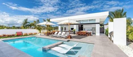 A modern house with a swimming pool, outdoor furniture, and palm trees.