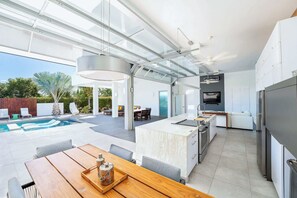 Una cucina moderna con isola centrale, un'area pranzo con tavolo in legno e una zona piscina con sedie a sdraio.