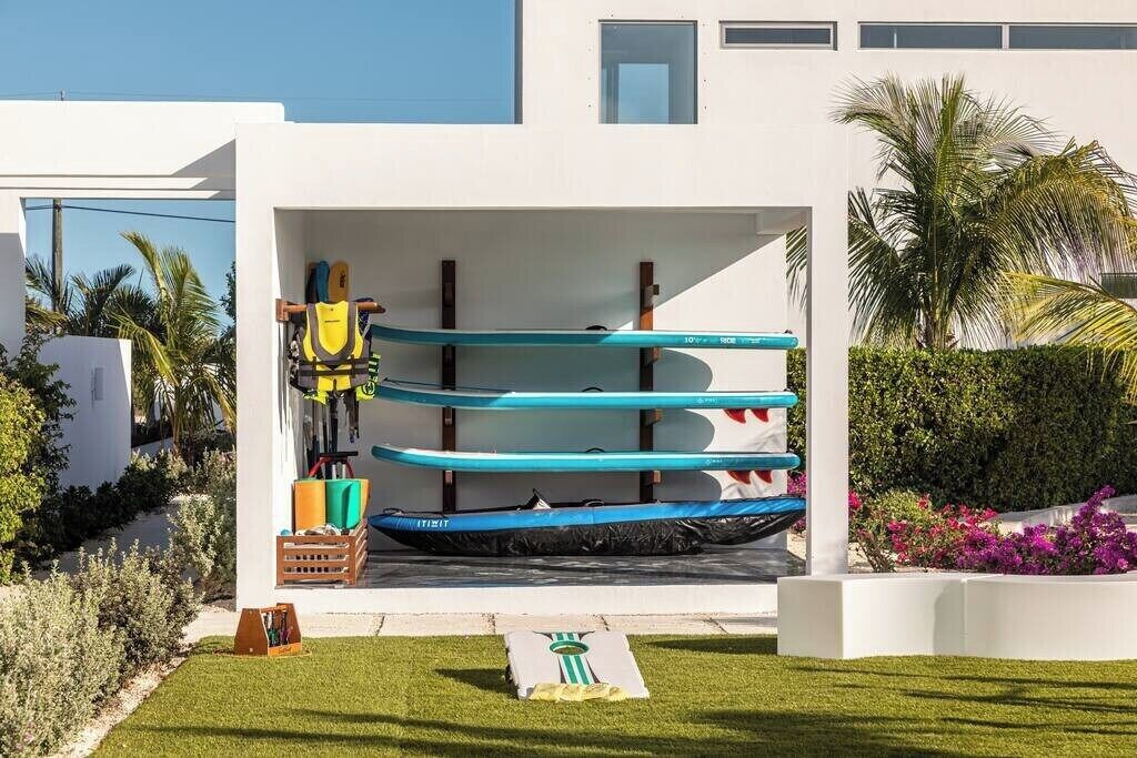 A modern building with a covered outdoor area containing several kayaks and a paddleboard.