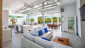 A modern open-plan living area with a kitchen, dining area, and a view of a swimming pool. - Vacation Villa, Oceanview and Hotel Amenities v1 (Providenciales)