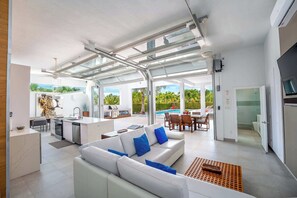 A modern open-plan living area with a kitchen, dining area, and a view of a swimming pool. - Vacation Villa, Oceanview and Hotel Amenities v1 (Providenciales)