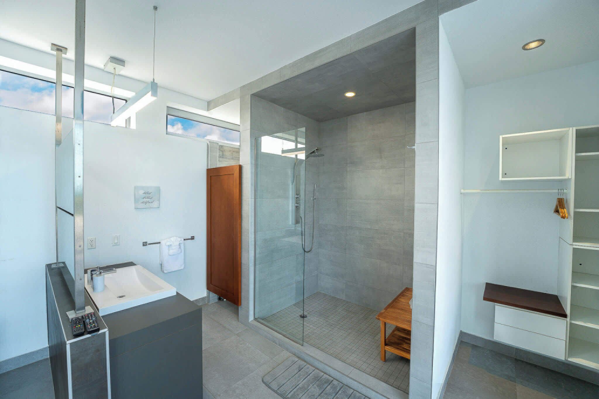 A modern bathroom with a glass-enclosed shower, a vanity with a sink, and a wooden bench.