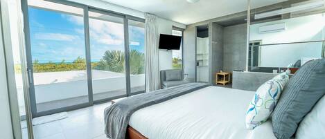 Un dormitorio moderno con una cama grande, un televisor de pantalla plana y un balcón con vista al océano.