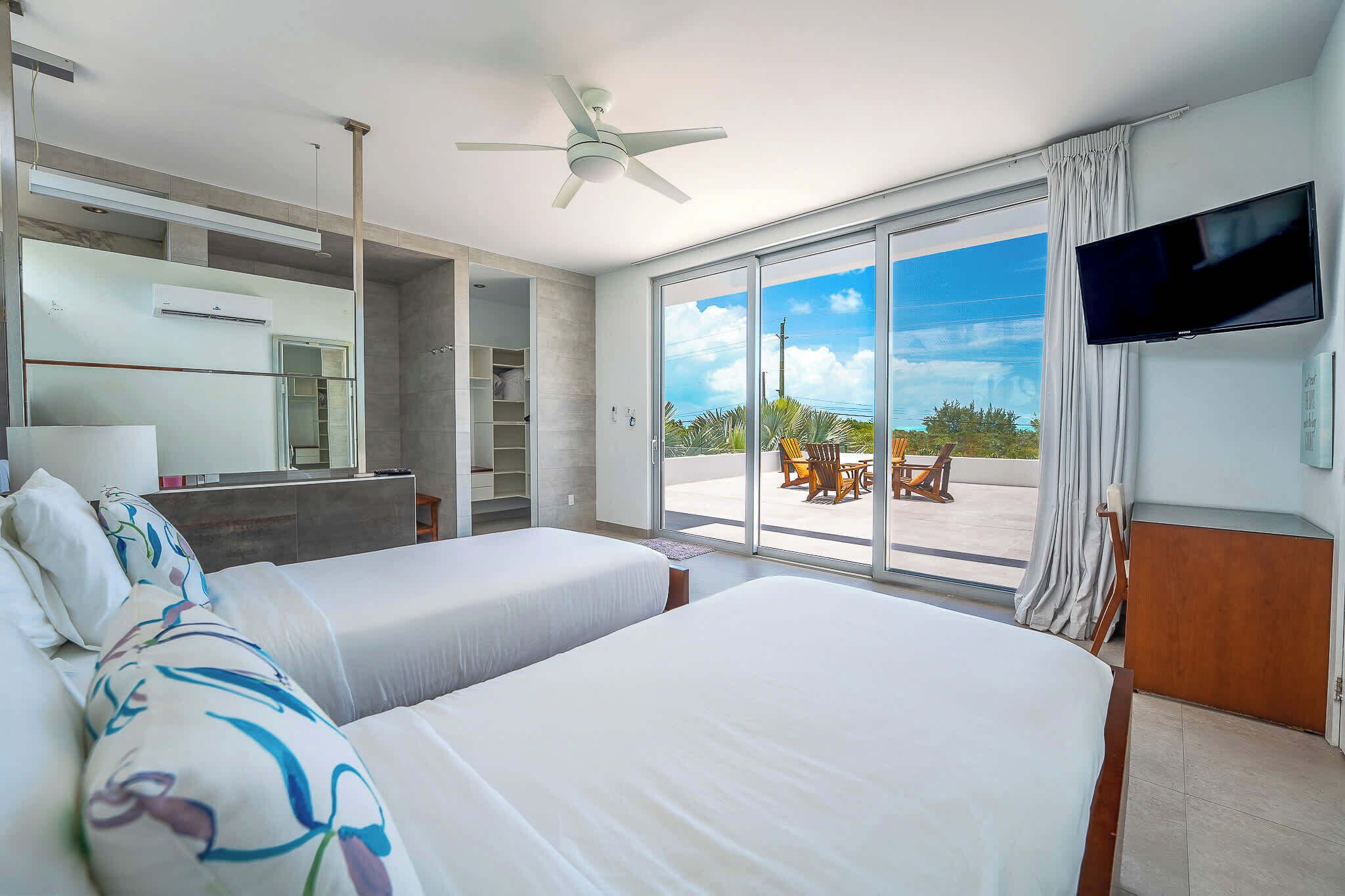 Une chambre d’hôtel avec deux lits, un ventilateur de plafond, une télévision et un balcon aménagé avec du mobilier d’extérieur.