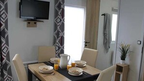 A dining area with a table set for breakfast, a television mounted on the wall, and a window with curtains.