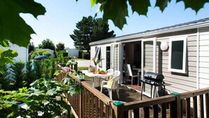 A mobile home with a deck, a grill, and a table with chairs.