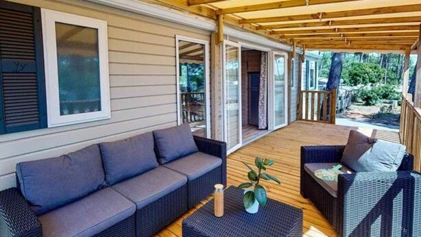 Un espace extérieur aménagé, abrité et doté d’un canapé et de fauteuils, d’un plancher en bois et d’une vue sur l’extérieur.
