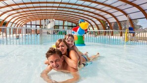 Un parc aquatique intérieur doté d’une piscine couverte, d’un toboggan et d’une grande décoration en forme de canard gonflable.
