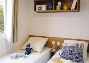 Quarto de hotel com uma cama, mesa de cabeceira, prateleira com recipientes de armazenamento e janela com cortinas.