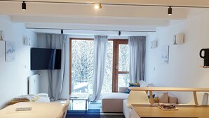 A modern hotel room with a dining table, a sofa, a TV mounted on the wall, and a view of a snowy landscape through the window. - Bright and spacious apartment for 6 people - View of the Flaine Forum (Arâches-la-Frasse)