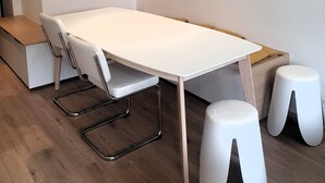 A modern room with a white table, two white stools, a wooden bench, and a white wall. - Bright and spacious apartment for 6 people - View of the Flaine Forum (Arâches-la-Frasse)