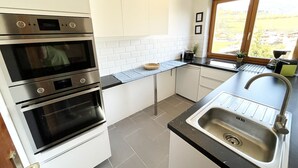 A modern kitchen with stainless steel appliances, a black countertop, and a window with a view of the outdoors. - Apartment Mountain Bliss (Kaprun)